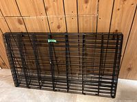 Folded black metal dog playpen panels leaning against wall.