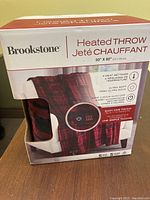 Photo of the front of the Brookstone Heated Throw box showing red and black plaid throw, 50 x 60 inches size, 4 heat settings, one-touch remote control and auto shutoff safety feature