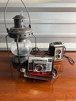 Metal lantern along with Kodak Brownie Reflex and Kodak Instamatic 314 cameras on a surface