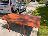 Midcentury modern teak dining table full view showing table top and legs outdoors on driveway.