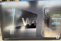 Front view of the Nintendo Wii box showing black console and Wii Remote controller, including branding and promotional info.
