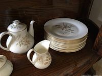 Photo showing stacked large dinner plates, teapot, creamer on a wooden shelf