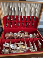 Full view of silverware set in wooden chest with red felt interior showing multiple forks, spoons, knives all with simple pattern.