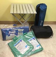 Photo showing aluminum folding table, two tarps in green plastic, one large tarp in blue package, sleeping bag, and air mattress packed in sacks