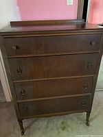 Full front view of antique tall boy dresser showing four drawers with metal ring handles and turned legs with casters.