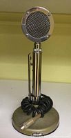 Front view of vintage Astatic D104 microphone showing round mesh grille and chrome cylindrical stem on weighted base with coiled cable.