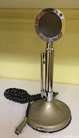Front view of vintage chrome Astatic Corp. microphone with mesh circular head on metallic stand base with attached cable.