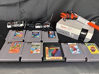 Original Nintendo Entertainment System console, two controllers, Zapper light gun, and 8 game cartridges arranged on black background showing labels and condition.
