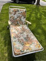 Photo showing the full lounger on green grass from above, displaying floral cushions and metal frame with wheels.