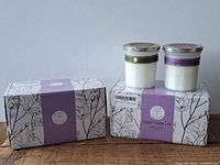 Two boxes of aromatherapy scented candles stacked with two candles outside the boxes showing jars and silver lids.