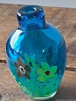 Photo of the front side showing blue glass vase with floral design and thick glass neck.