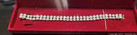 Full length view of the silver toned bracelet resting on red velvet background, showing its slender design and uniform crystal setting.