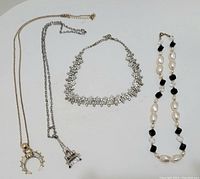Full view of four necklaces including crescent pendant, Eiffel Tower pendant, rhinestone floral necklace, and pearl and black bead necklace.