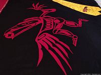 Close-up of red stylized bird motif on black cloth with magenta border