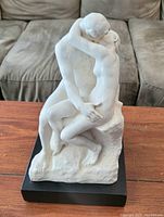 Front view of white sculpture The Kiss showing nude embracing couple on black base.