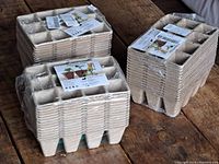Stacks of biodegradable pulp seed starter trays sealed in plastic wrap, stacked on a wooden surface.
