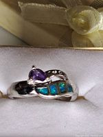 Close-up of the sterling silver ring featuring a pear-shaped amethyst and three blue-green opal inlays in a white box.