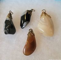 Photo of four irregularly shaped stone pendants with metal caps and loops on a light background.