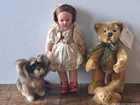 Lot showing all four items: vintage doll, teddy bear with ribbon and tag, and two small animal figurines