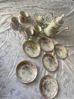 Photo showing arrangement of the 12-piece RS porcelain tea set, including cups, saucers, teapot, sugar bowl, and creamer with floral designs and gold rim.