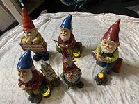 Five garden gnomes on a white sheet; various poses, some with solar features, some with paint chips and cracks.