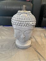 Front view of Buddha head tiki torch decoration in gray ceramic-style material, showing overall structure and torch attachment.