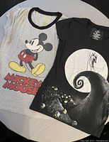 Two Disney-themed t-shirts laid flat showing front graphics and designs.