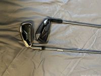 Two golf irons laid on a fabric surface, showing metal club heads and grips, illustrating one left-handed and one right-handed club.