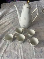 Porcelain teapot with handle, spout, gold accents, and five matching teacups arranged on a cloth surface with butterfly pattern.