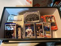Wide shot showing box filled with various hockey and baseball sports cards including cards of Felix Potvin, Nolan Ryan, Cam Neely, and a black-and-white team photo.