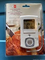 Front side of sealed packaging showing white digital roasting thermometer with fold-up LCD screen and round dial controls over photo of roast chicken.