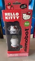 Front view of Hello Kitty USB flash drive in original red packaging showing 4GB capacity and Mimobot branding.