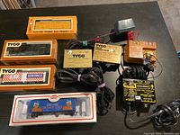 HO scale toy train cars in original boxes and multiple TYCO and GP Train transformers and power packs on a flat surface.