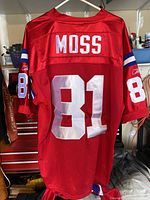 Back view of red jersey showing 'MOSS' and number '81' in white block letters and numbers with blue and white stripes on sleeves.