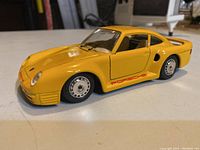 Side view of yellow Porsche 959 diecast model car on a flat surface showing detailed decals and tires.