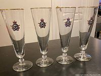Four RCAF commemorative pilsner glasses standing upright on a dark surface, showing the RCAF emblem and gold rim.