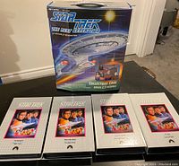 Photo of the Star Trek The Next Generation collector case along with 4 VHS tapes laid out in front of it, clearly showing cover art and packaging style.