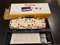 Tile rummy game box open showing tiles in the tray, instruction sheet, and tile racks.