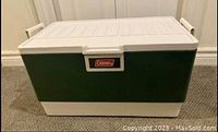Closed front view of vintage green and white Coleman cooler showing front brand label and side handles.