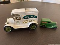 Wide view of the white Heinz 57 Varieties diecast delivery truck and a smaller green diecast van side by side on a wooden surface.