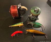 Photo of two vintage fishing reels and four fishing lures showing details of wear and color.