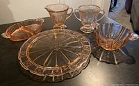 Five pieces of vintage rose glassware displayed on dark table including serving plate, divided dish, creamer, sugar bowl, handled bowl.