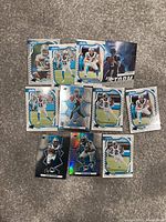 Photo showing 10 Carolina Panthers NFL trading cards laid out on carpet, featuring various players in action poses, some cards holographic.