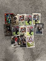 Photo shows 12 NFL trading cards arranged on gray carpet including New Orleans Saints players mostly, with different card brands and holographic effects visible.