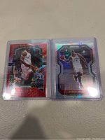 Two Serge Ibaka basketball trading cards in clear protective sleeves, one red-themed and the other holographic silver-themed.