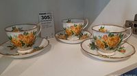 Three Royal Albert Tea Rose pattern bone china tea cups paired with matching saucers, displayed on shelf.