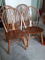 Four wooden dining chairs with spindle backs arranged together showing shape and condition.