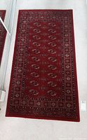 Full view of the rectangular traditional red Turkish rug lying flat on a carpeted floor.