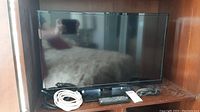 Front view of Insignia 32-inch TV on its stand with cables and remote control placed in front.