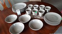 Sets of stacked large plates, bowls, and cups displayed on a wooden table showing the overall quantity and condition